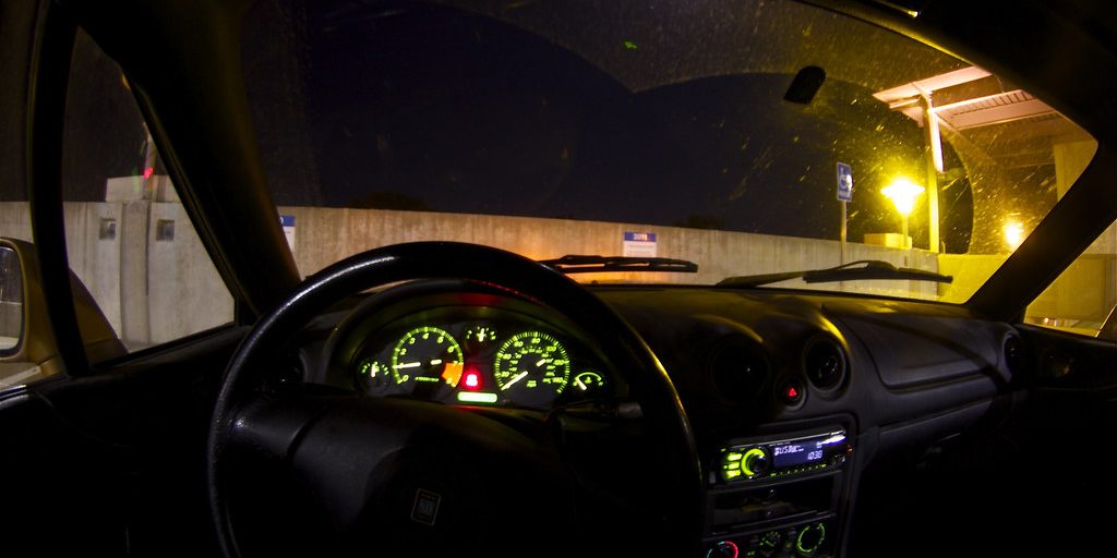 The lit instrument panel of a car seen from the driver's seat at night