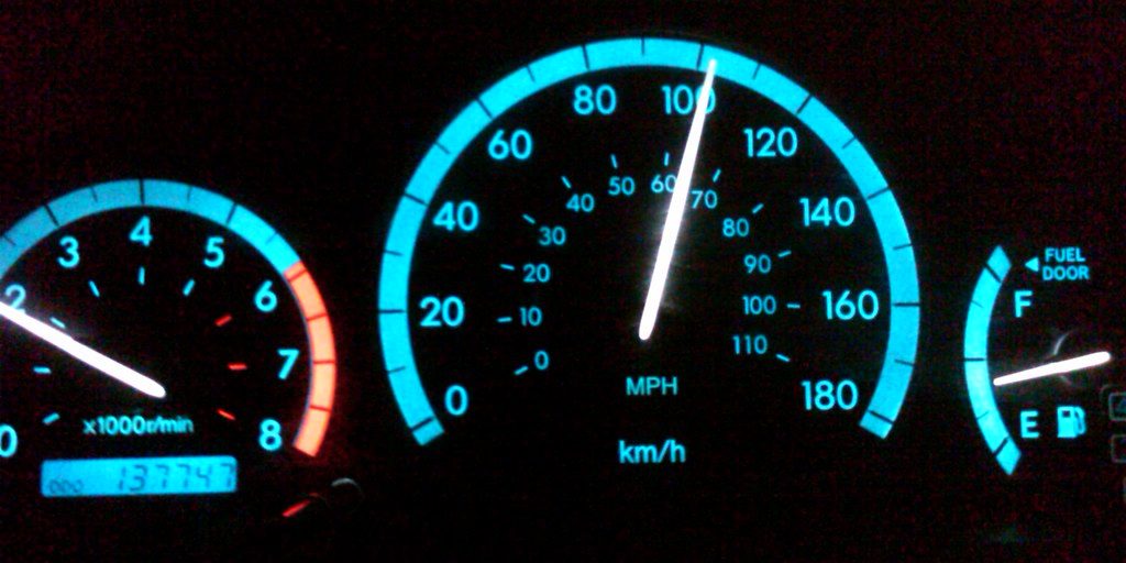 A lit car instrument cluster at night showing the speedometer, rev counter and odometer